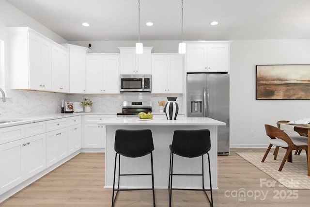 1815 Wildwood Dr, Charlotte, NC 28214 - kitchen with stainless steel appliances, a breakfast bar area, tasteful backsplash, light wood finished floors, and white cabinets