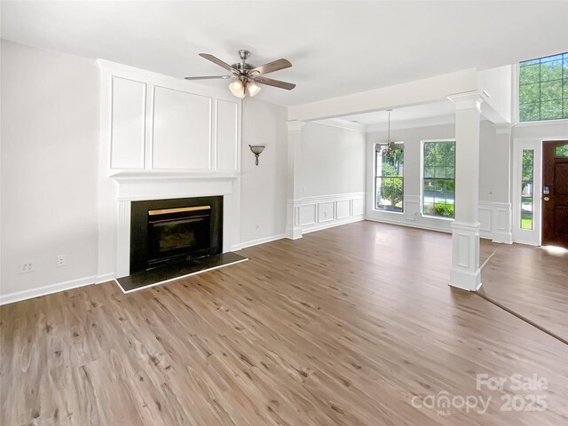 6413 Fillian Ln, Charlotte, NC 28269 - unfurnished living room featuring a decorative wall, healthy amount of natural light, ornate columns, light wood-style flooring, and wainscoting