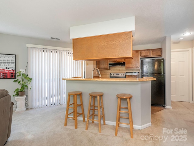 8208 Cedar Glen Dr, Charlotte, NC 28212 - kitchen featuring freestanding refrigerator, under cabinet range hood, light carpet, and a breakfast bar area