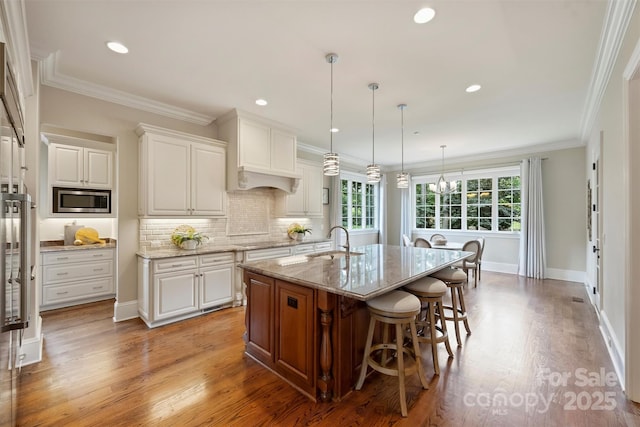 3032 Kings Manor Dr, Matthews, NC 28104 - kitchen with stainless steel microwave, light stone counters, light wood-type flooring, a breakfast bar area, and white cabinets
