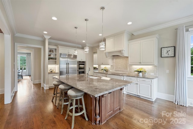 3032 Kings Manor Dr, Matthews, NC 28104 - kitchen featuring built in refrigerator, wood finished floors, a center island with sink, tasteful backsplash, and a kitchen bar