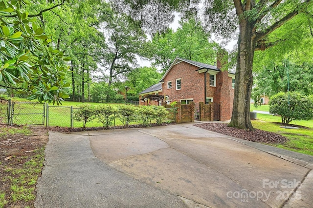 2301 Seth Thomas Rd, Charlotte, NC 28210 - view of home's exterior with a gate, a chimney, brick siding, concrete driveway, and view of wooded area