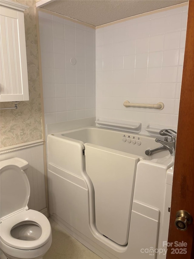 550 Camrose Cir NE, Concord, NC 28025 - full bathroom with wallpapered walls, a wainscoted wall, a tub to relax in, toilet, and a textured ceiling