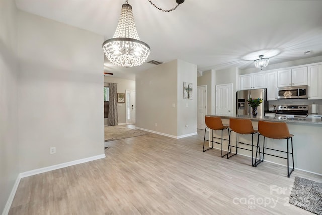 7931 Baylis Dr, Huntersville, NC 28078 - kitchen featuring stainless steel appliances, a chandelier, a kitchen bar, white cabinets, and light wood-type flooring