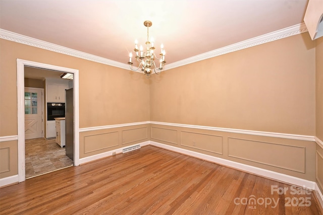 1961 Runnymede Ln, Charlotte, NC 28211 - unfurnished room with a chandelier, a decorative wall, ornamental molding, light wood-style flooring, and a wainscoted wall
