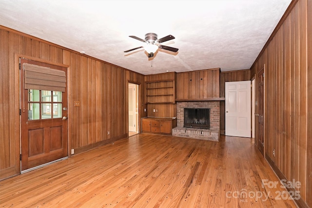 1961 Runnymede Ln, Charlotte, NC 28211 - unfurnished living room featuring wood walls, a ceiling fan, a fireplace, light wood-style flooring, and built in shelves