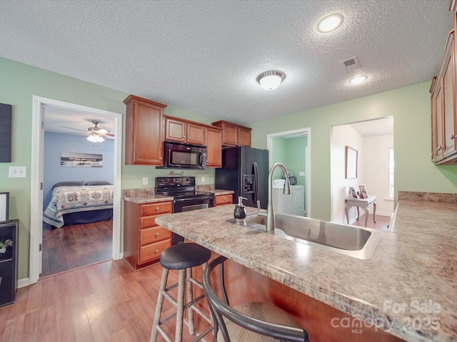 1060 S Lentz Harness Shop Rd, Mount Pleasant, NC 28124 - kitchen with black appliances, a kitchen bar, a sink, light wood-style floors, and a textured ceiling
