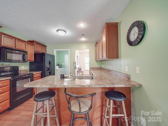1060 S Lentz Harness Shop Rd, Mount Pleasant, NC 28124 - kitchen with black appliances, a sink, a textured ceiling, a peninsula, and light wood finished floors