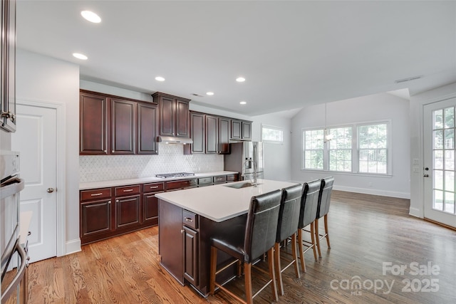 2785 Disney Pl, Indian Land, SC 29707 - kitchen with appliances with stainless steel finishes, under cabinet range hood, light wood finished floors, a breakfast bar, and light countertops