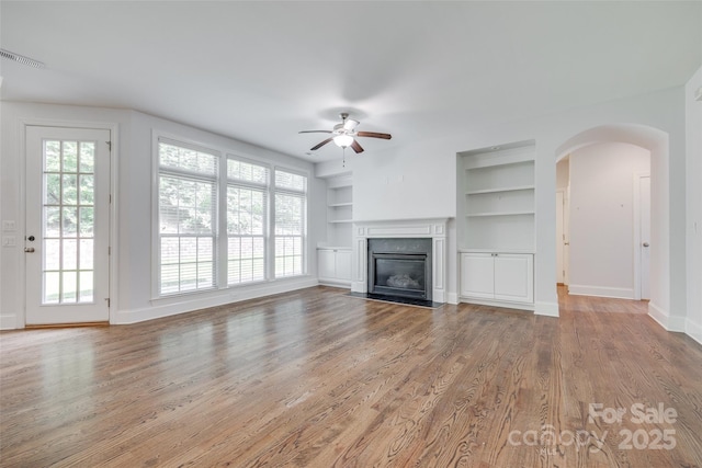 2785 Disney Pl, Indian Land, SC 29707 - unfurnished living room with a ceiling fan, built in shelves, arched walkways, wood finished floors, and a fireplace