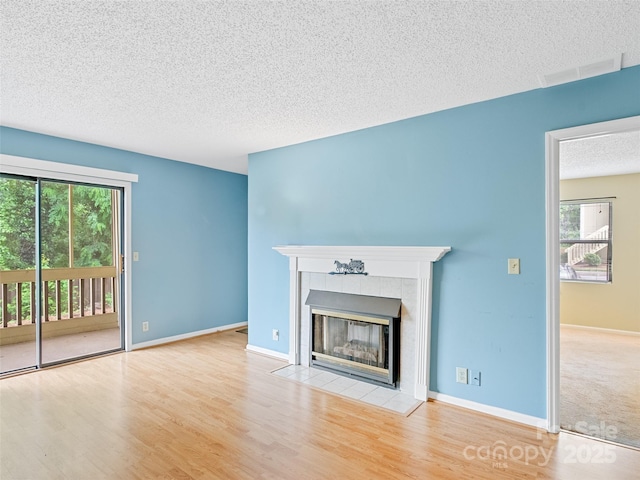 110 Heywood Rd Unit 17C, Arden, NC 28704 - unfurnished living room featuring a textured ceiling, plenty of natural light, a tiled fireplace, wood finished floors, and baseboards