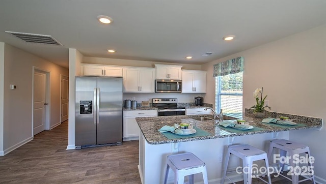 5137 Hyrule Dr, Charlotte, NC 28262 - kitchen featuring stainless steel appliances, dark stone counters, dark wood-style flooring, a sink, and white cabinetry