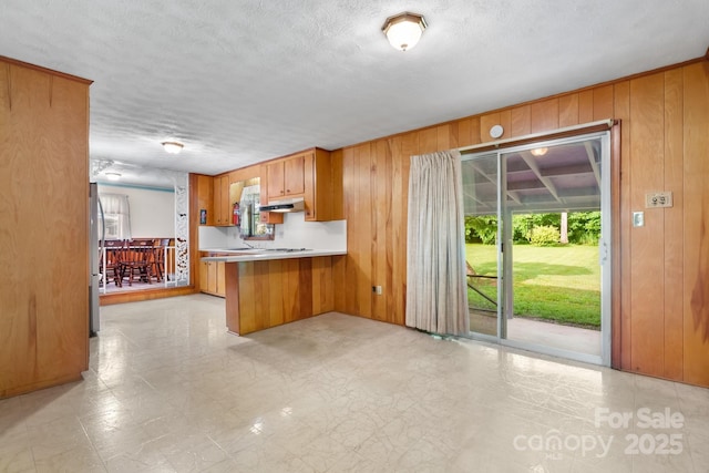 518 W School St, Maiden, NC 28650 - kitchen with wood walls, brown cabinets, under cabinet range hood, freestanding refrigerator, and a peninsula