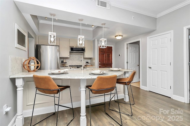 300 W 5th St Unit 003, Charlotte, NC 28202 - kitchen featuring appliances with stainless steel finishes, crown molding, backsplash, light wood-style flooring, and a breakfast bar area