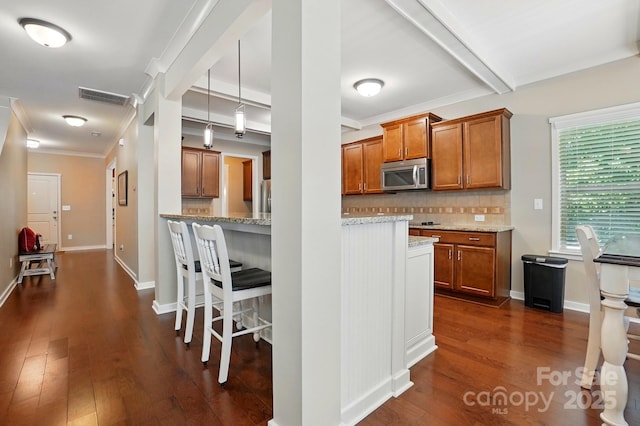 3106 Crosswind Dr, Fort Mill, SC 29707 - kitchen featuring stainless steel microwave, brown cabinetry, dark wood finished floors, backsplash, and ornamental molding
