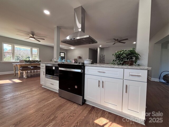 8607 Larchmont Cir, Charlotte, NC 28214 - kitchen featuring island exhaust hood, range with electric cooktop, stainless steel microwave, ceiling fan, and white cabinetry