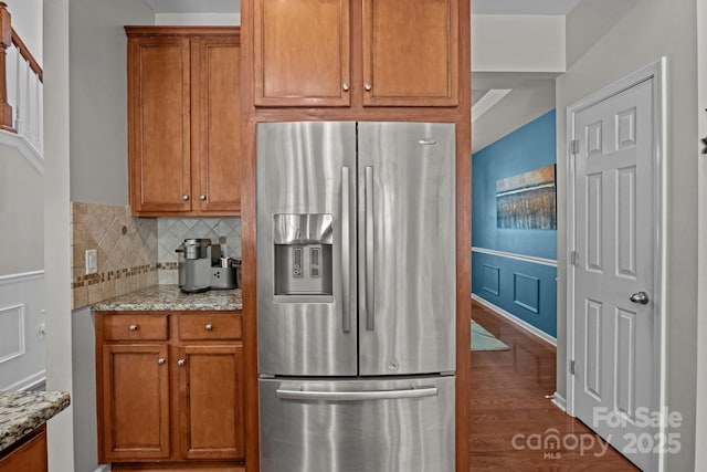 2233 Sonoma Valley Dr, Charlotte, NC 28214 - kitchen featuring stainless steel fridge with ice dispenser, brown cabinets, light stone countertops, dark wood-type flooring, and a wainscoted wall