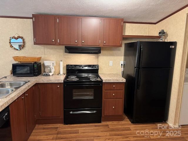 kitchen with black appliances, under cabinet range hood, a textured ceiling, a sink, and light countertops