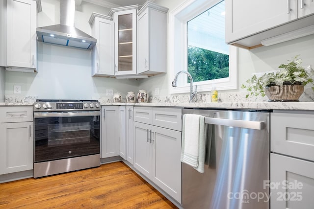 219 Grayson St, Sparta, NC 28675 - kitchen with appliances with stainless steel finishes, wall chimney exhaust hood, glass insert cabinets, light wood finished floors, and light stone countertops