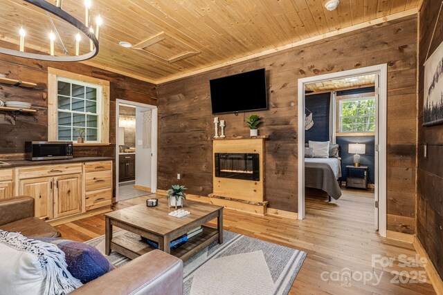 6541 Grassy Branch Rd, Bryson City, NC 28713 - living area featuring wooden ceiling, wooden walls, attic access, light wood-style floors, and a glass covered fireplace