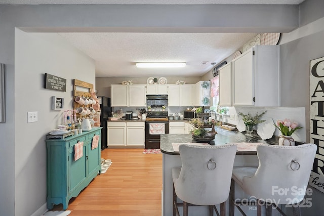 1912 8th St SE, Hickory, NC 28602 - kitchen with black appliances, a peninsula, light wood-style floors, a kitchen bar, and white cabinets
