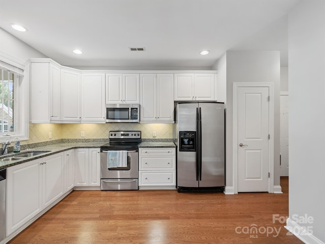 10875 Casetta Dr, Matthews, NC 28105 - kitchen with appliances with stainless steel finishes, light wood-style flooring, white cabinets, tasteful backsplash, and dark stone countertops