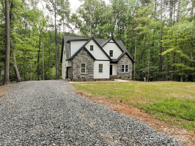248 Pioneer Dr, Mount Gilead, NC 27306 - view of front facade featuring gravel driveway, stone siding, a shingled roof, and a forest view