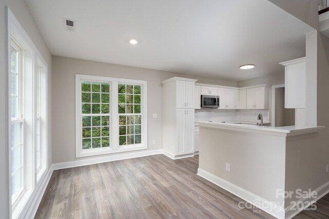 248 Pioneer Dr, Mount Gilead, NC 27306 - kitchen featuring stainless steel microwave, white cabinetry, light countertops, tasteful backsplash, and wood finished floors
