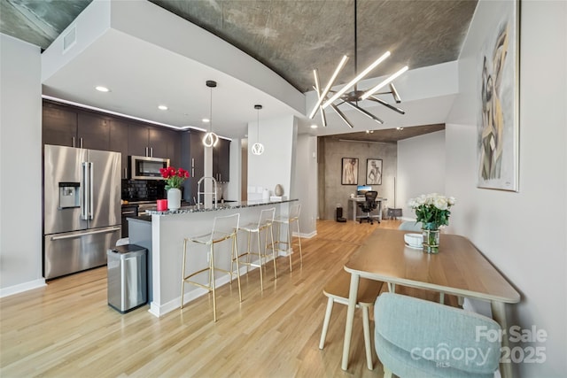210 N Church St Unit 2807, Charlotte, NC 28202 - kitchen with stainless steel appliances, light wood-style flooring, a breakfast bar area, dark brown cabinetry, and backsplash