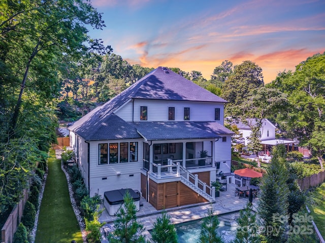 4211 Tangle Dr, Charlotte, NC 28211 - back of house at dusk with a patio, a sunroom, a shingled roof, a jacuzzi, and stairs