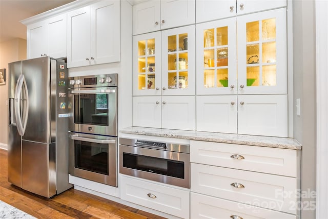 1868 Chestnut Hill Dr, Tega Cay, SC 29708 - kitchen featuring stainless steel appliances, wood finished floors, white cabinetry, glass insert cabinets, and light stone counters