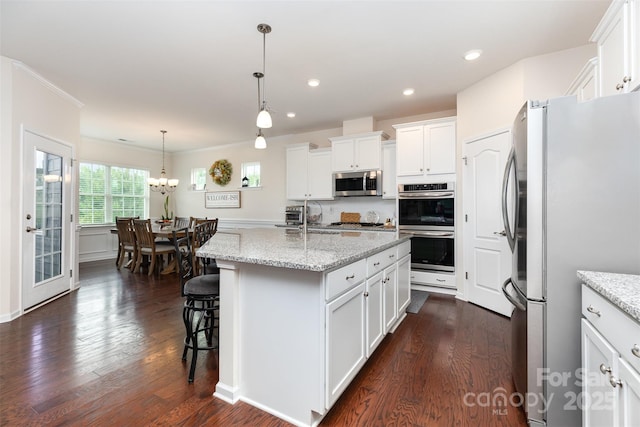 1663 Tranquility Blvd, Lancaster, SC 29720 - kitchen featuring appliances with stainless steel finishes, dark wood-style flooring, white cabinetry, a center island with sink, and light stone countertops