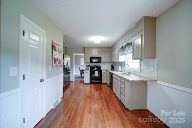 734 Forestbrook Dr, Gastonia, NC 28056 - kitchen featuring black appliances, light wood-style floors, a wainscoted wall, tasteful backsplash, and a decorative wall