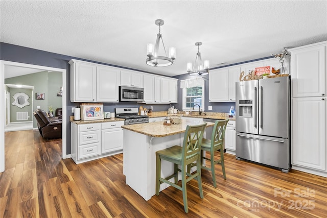 106 Laren Rd, Shelby, NC 28152 - kitchen with appliances with stainless steel finishes, a chandelier, white cabinetry, wood finished floors, and a textured ceiling