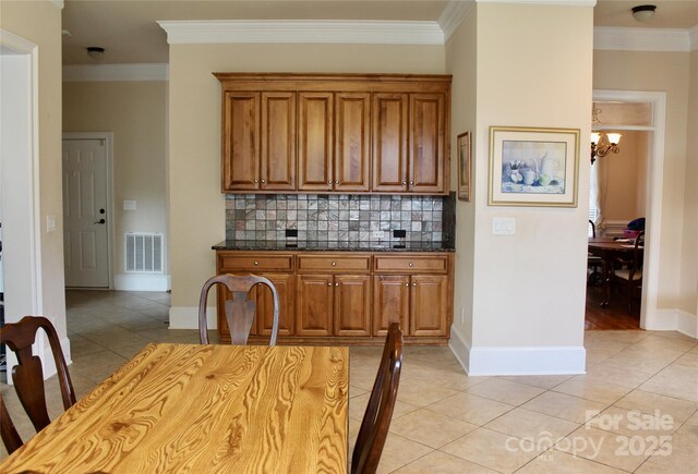 8620 Rolling Fields Rd, Charlotte, NC 28227 - kitchen featuring brown cabinets, a chandelier, crown molding, tasteful backsplash, and light tile patterned floors