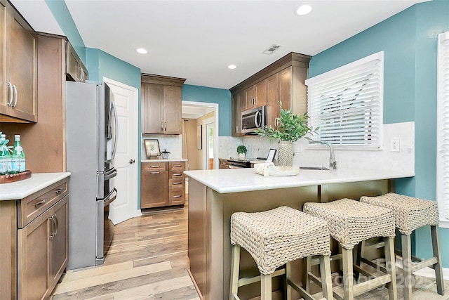 1011 Bydeford Ct, Matthews, NC 28105 - kitchen featuring stainless steel appliances, a sink, a peninsula, light wood-style floors, and decorative backsplash