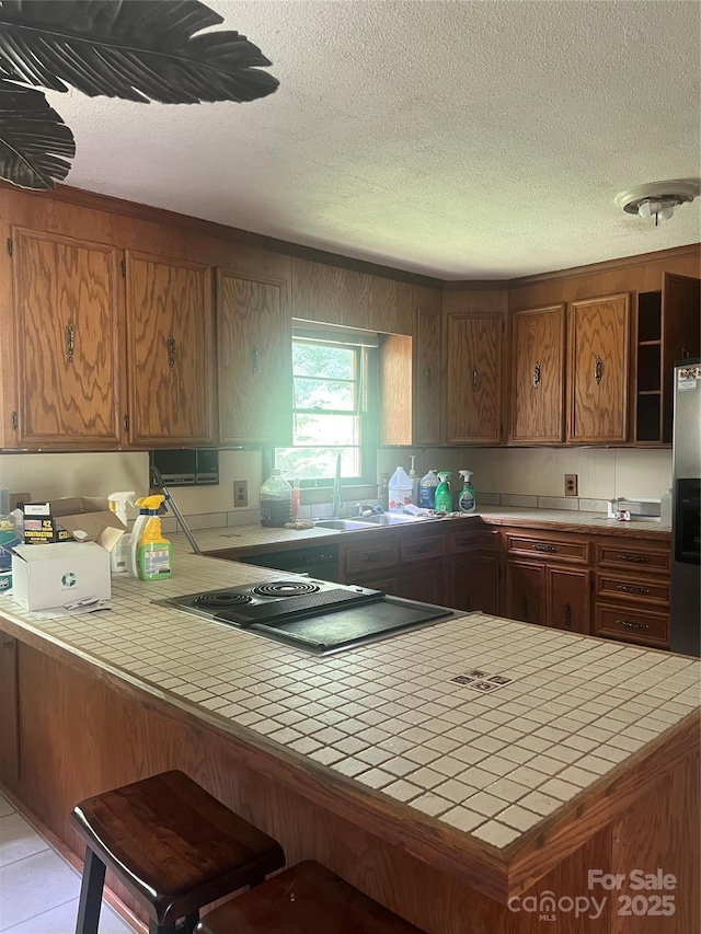 168 Pleasant Creek Dr, Cleveland, NC 27013 - kitchen featuring tile countertops, a textured ceiling, brown cabinetry, a breakfast bar, and a peninsula