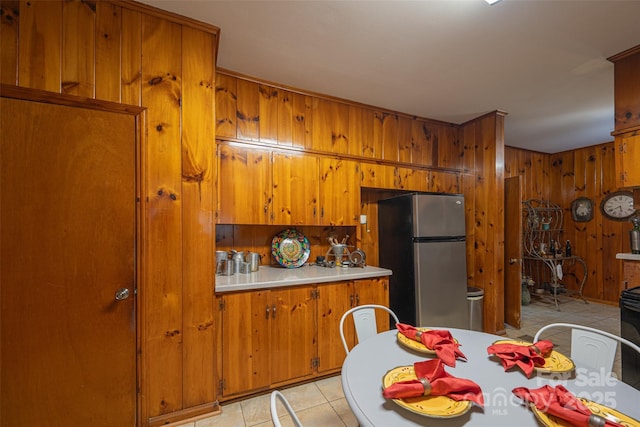 100 S Rudisill Ave, Cherryville, NC 28021 - kitchen featuring freestanding refrigerator, brown cabinets, wood walls, light tile patterned floors, and light countertops