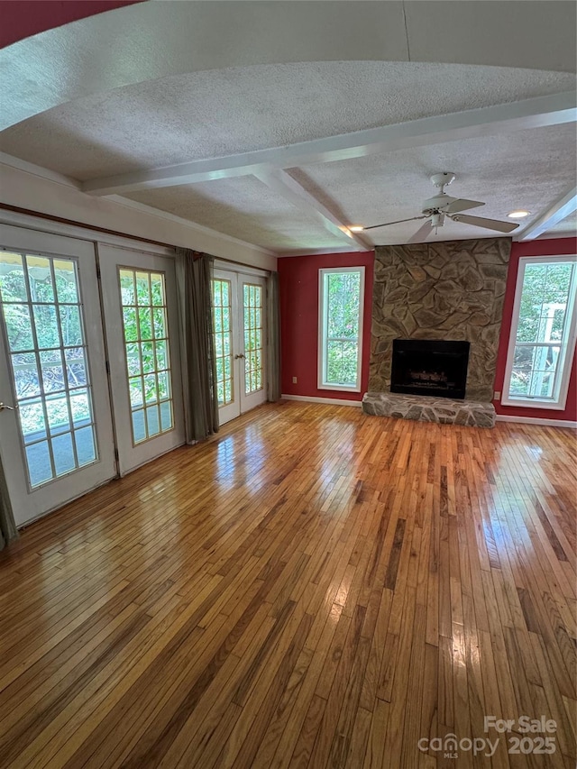 232 Cole Hollow Rd, Newland, NC 28657 - unfurnished living room with a textured ceiling, wood-type flooring, a stone fireplace, ceiling fan, and beamed ceiling