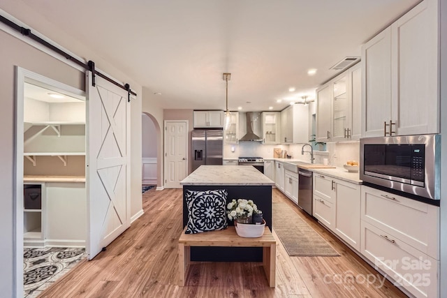 7810 Leisure Ln, Huntersville, NC 28078 - kitchen with stainless steel appliances, wall chimney exhaust hood, a center island, a barn door, and light wood-type flooring
