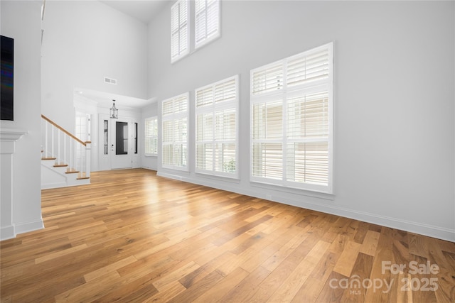 3008 Laney Pond Rd, Matthews, NC 28104 - unfurnished living room featuring a towering ceiling, light wood finished floors, stairway, and baseboards