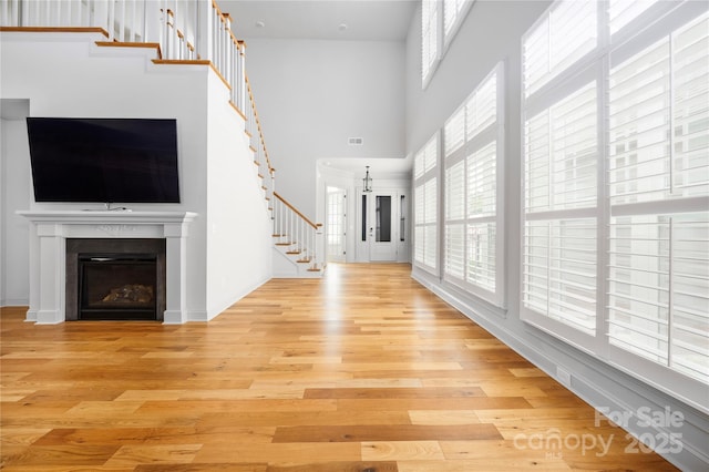 3008 Laney Pond Rd, Matthews, NC 28104 - unfurnished living room with a high ceiling, light wood finished floors, stairway, and a glass covered fireplace