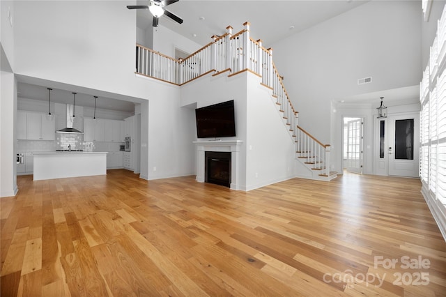 3008 Laney Pond Rd, Matthews, NC 28104 - unfurnished living room with a high ceiling, a glass covered fireplace, light wood-type flooring, ceiling fan, and stairway