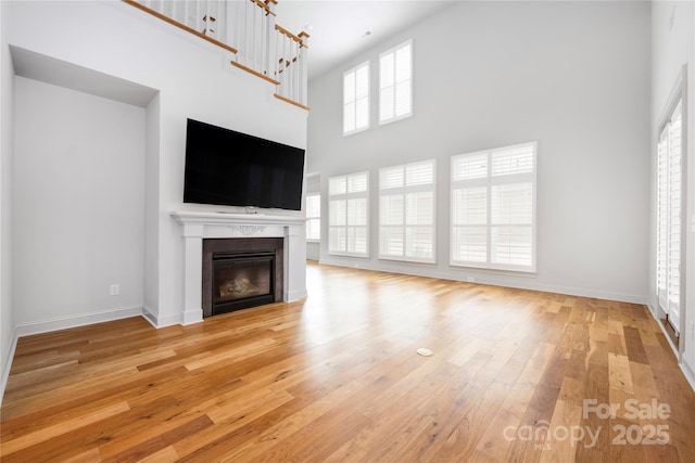 3008 Laney Pond Rd, Matthews, NC 28104 - unfurnished living room with a towering ceiling, light wood-style floors, a glass covered fireplace, and baseboards