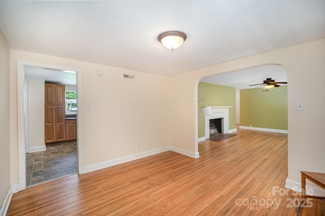 409 Edgewood Ct, Lancaster, SC 29720 - unfurnished room with arched walkways, a ceiling fan, light wood-style floors, and a fireplace with flush hearth