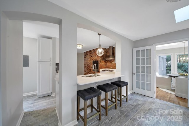 3800 Lovett Cir, Charlotte, NC 28210 - kitchen with wall chimney exhaust hood, wood finished floors, a kitchen bar, hanging light fixtures, and a skylight