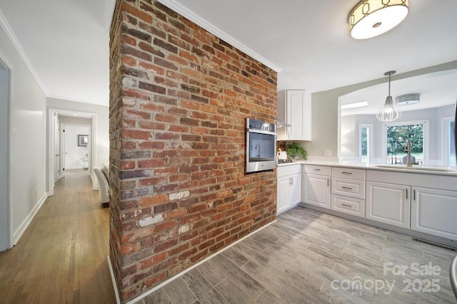3800 Lovett Cir, Charlotte, NC 28210 - kitchen featuring light wood finished floors, stainless steel oven, white cabinetry, ornamental molding, and brick wall