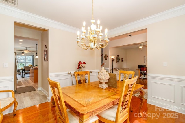 1006 Apogee Dr, Indian Trail, NC 28079 - dining space featuring a ceiling fan, light wood finished floors, crown molding, a wainscoted wall, and a chandelier