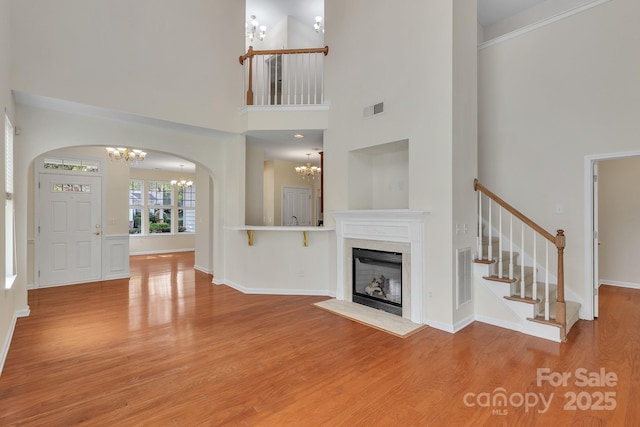 5963 Pale Moss Ln, Charlotte, NC 28269 - unfurnished living room featuring a chandelier, arched walkways, light wood-style floors, a towering ceiling, and stairway