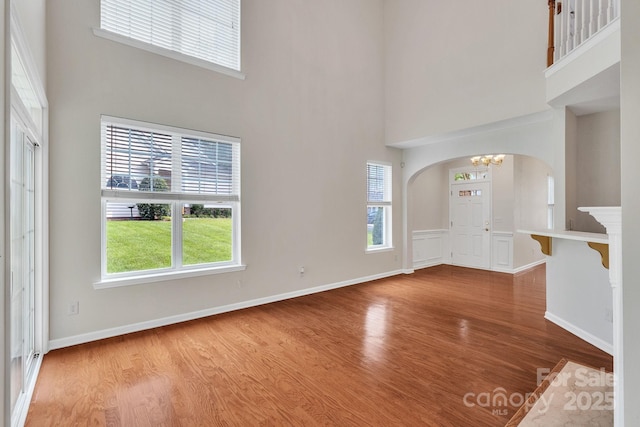 5963 Pale Moss Ln, Charlotte, NC 28269 - unfurnished living room featuring arched walkways, a high ceiling, wood finished floors, healthy amount of natural light, and a chandelier